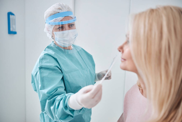 Professional nurse screening a woman for COVID-19 - Фото, изображение