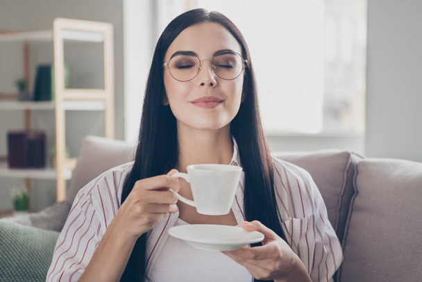 Portrait photo of brunette woman drinking coffee smelling aroma with closed eyes keeping mug at home - Photo, Image