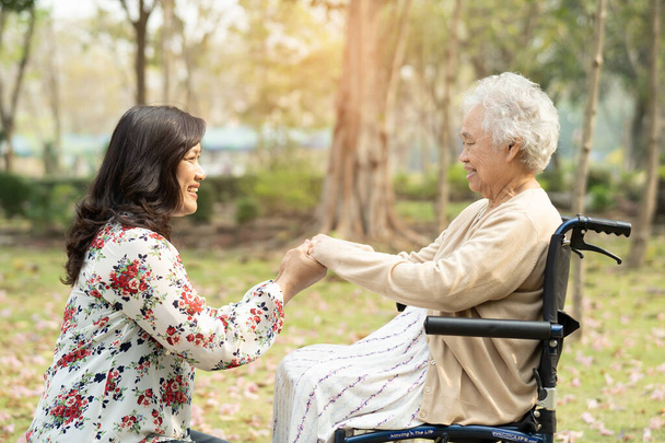 Aînée asiatique ou vieille dame âgée patiente avec des soins, de l'aide et du soutien en fauteuil roulant dans le parc en vacances, concept médical fort sain.  - Photo, image
