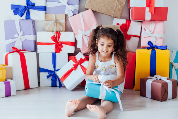 Маленькая кудрявая веселая девочка и куча подарков на день рождения - Фото, изображение