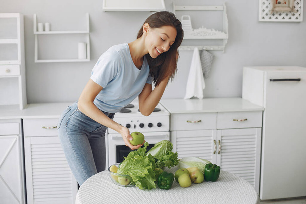 Beautiful and sporty girl in a kitchen with a vegetables - Foto, afbeelding