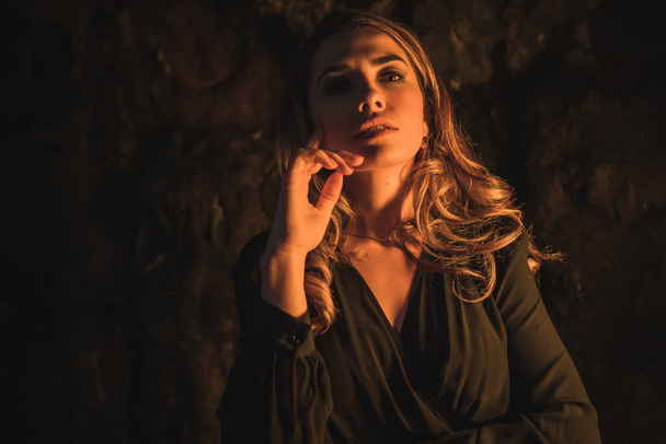Lifestyle, a young Caucasian blonde in a black dress in a photo inside a cave, illuminated with yellow light. Portrait of the young woman enjoying the autumn afternoon - Foto, immagini