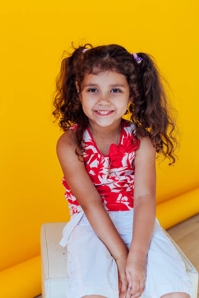 Mooi klein krullend vrolijk meisje met vlechten op een gele achtergrond - Foto, afbeelding