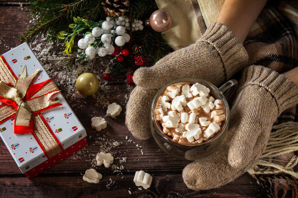 Руки женщины варежки рождественские подарки и горячий какао с зефиром на деревянном столе. - Фото, изображение