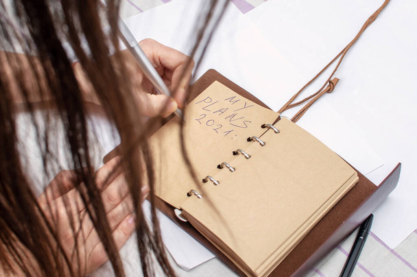 Primer plano estilo de vida de una mujer joven, hace un plan para el futuro 2021 en un cuaderno vintage. Vista desde atrás, en el marco, cabello. - Foto, Imagen