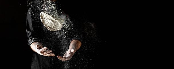 flying pizza dough with flour scattering in a freeze motion of a cloud of flour midair on black. Cook hands kneading dough. copy space. - Photo, Image