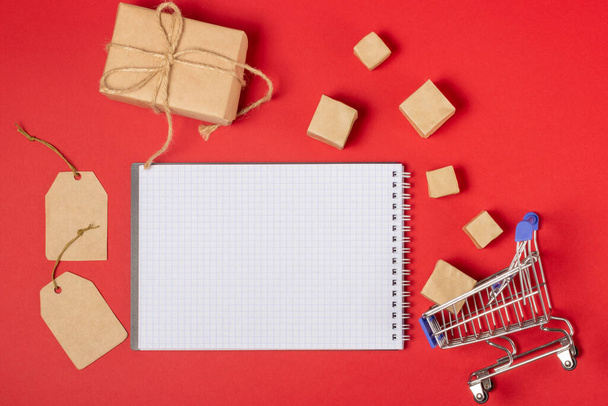 Open blank notebook with place to add text, shopping cart and boxes on a bright red background. Online shopping concept - Photo, image