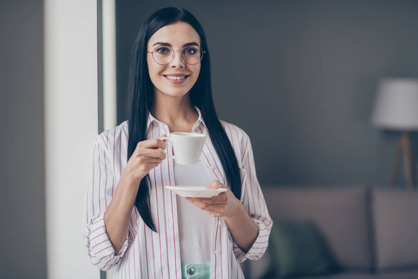 Photo portrait of woman drinking coffee tea holding white cup plate in hands indoors - Foto, Bild