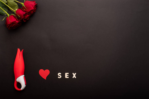 Top view of roses, clitoral vibrator in the form of a red tulip, heart and the inscription clitoris on a black background. Flat lay. Copy space - Фото, зображення
