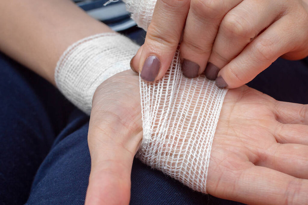 Una joven venda su mano lesionada con un vendaje de gasa blanca. Primer plano - Foto, Imagen