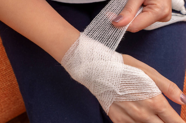 Die junge Frau bandagiert ihr Handgelenk selbstständig. Nahaufnahme, Draufsicht, warme Tönung - Foto, Bild