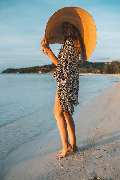 Portrait of a woman posing on the beach. Attractive female wearing black swimsuit and big fashionable hat. - Foto, Imagem