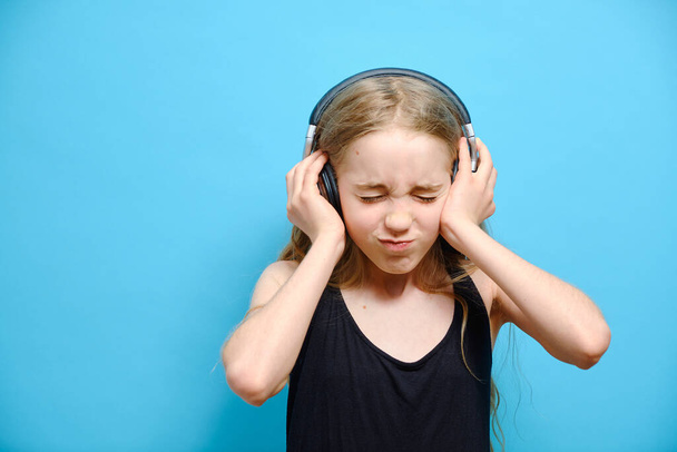 Little caucasian girl in headphones closed her eyes on a blue background. Emotions concept. - Foto, Bild