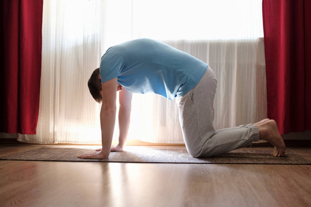 man practices yoga asana marjariasana or cow pose at home. - Photo, Image
