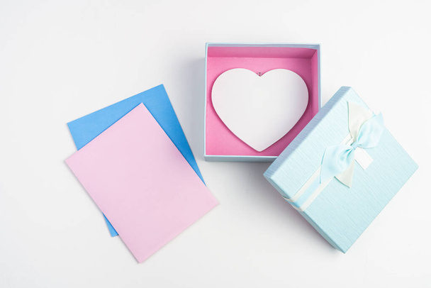 Růžové a modré obálky a dárková krabice s bílým srdcem na světlém pozadí. - Fotografie, Obrázek