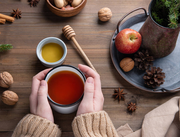 As mãos guardam a xícara do Natal de aroma Chá de maçã com a canela em uma mesa de madeira. Vista superior - Foto, Imagem