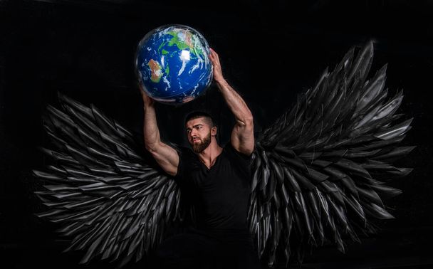 красивий м'язистий чоловік в костюмі ангела з чорними крилами на чорному тлі
 - Фото, зображення