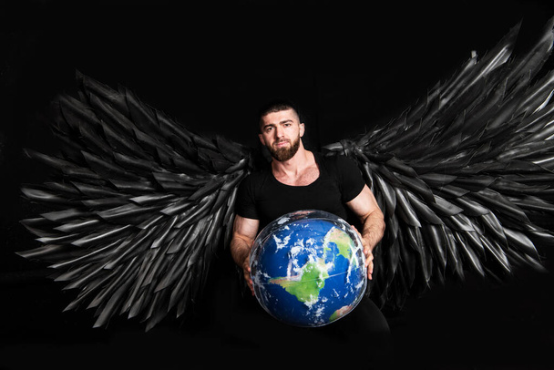 przystojny muskularny mężczyzna w anioł kostium z czarnymi skrzydłami na czarnym tle - Zdjęcie, obraz