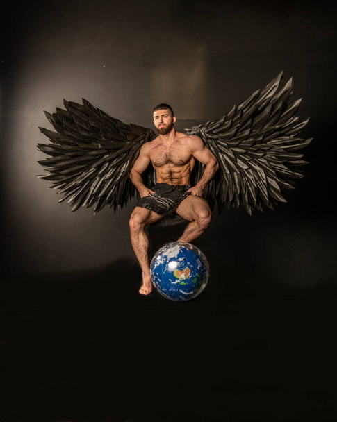 przystojny muskularny mężczyzna w anioł kostium z czarnymi skrzydłami na czarnym tle - Zdjęcie, obraz