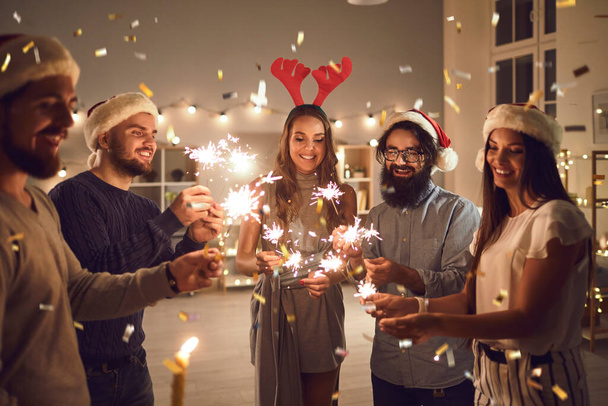 Smiling friends with sparklers wishing each other Merry Christmas and Happy New Year at home party - 写真・画像
