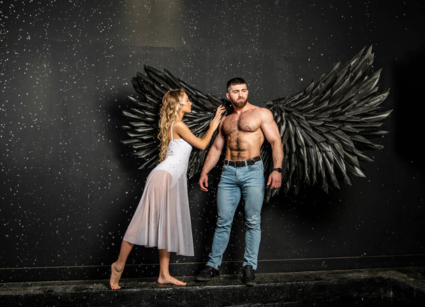 красивий м'язистий чоловік в костюмі ангела з чорними крилами і тендітна беззахисна красива дівчина в білому
 - Фото, зображення