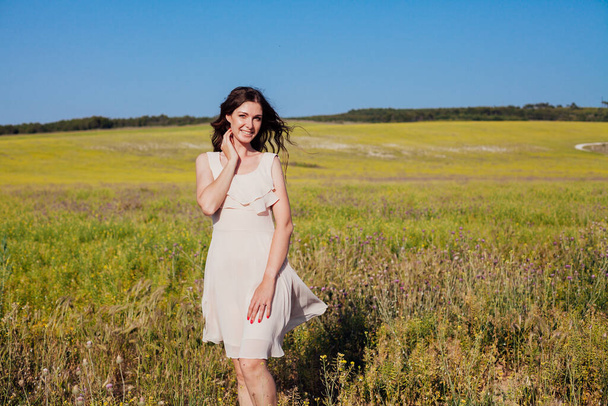 Retrato de una hermosa mujer de moda en un vestido en un campo con flores amarillas - Foto, Imagen