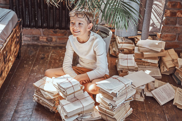 Fröhliches Kind sitzt in Wohnung um Bücher herum auf dem Boden - Foto, Bild