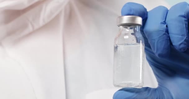 Ученый в синих нитрильных перчатках держит грипп, корь, коронавирусную бутылку вакцины в лаборатории - Кадры, видео