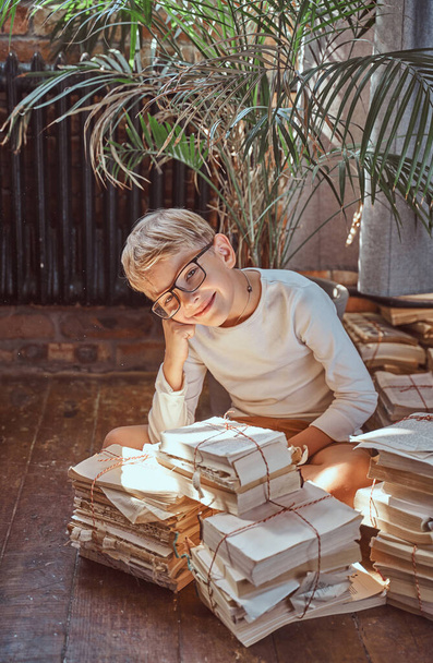 Fröhliches Kind sitzt in Wohnung um Bücher herum auf dem Boden - Foto, Bild