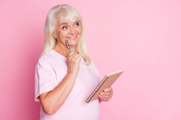 Photo portrait of dreamy woman touching cheek face with pen holding notepad isolated on pastel pink colored background - Φωτογραφία, εικόνα