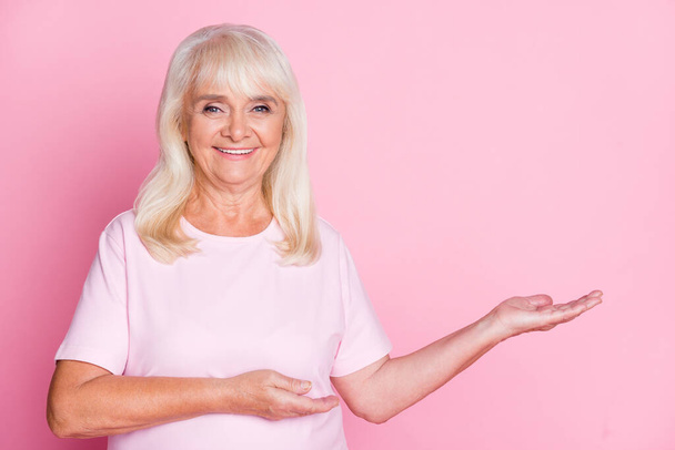Photo portrait of happy old lady holding blank space in hands isolated on pastel pink colored background - Foto, immagini
