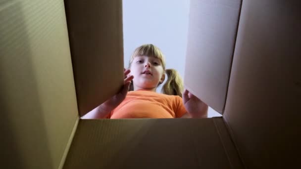Das Kind öffnete eine Schachtel mit einem Geschenk. Ein kleines Mädchen schaut in die Box, ist überrascht und freut sich über eine Überraschung. Zeitlupe. - Filmmaterial, Video