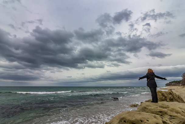 Una mujer en la cima de una roca disfruta de la vista del mar y el cielo nublado - Foto, imagen