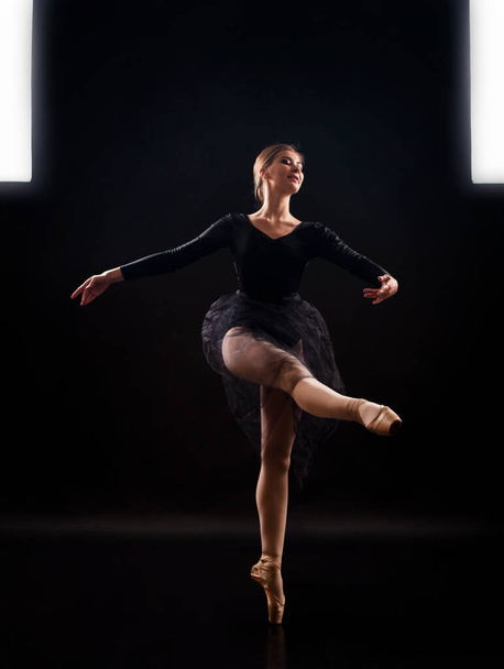 Charming girl ballerina in a black suit, is dancing a ballet in the light of the contour . Shooting a performance on a dark background. - Fotó, kép