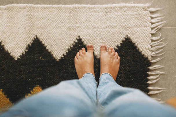 Feet on cozy woolen rug on background of concrete floor. Woman barefoot standing on modern rug in comfortable stylish home, top view. Cozy warm moments - Photo, Image