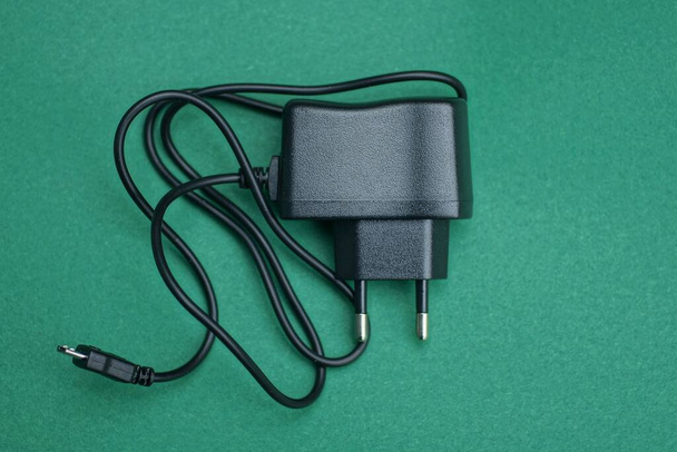 один чорний пластиковий зарядний пристрій лежить на зеленому столі
 - Фото, зображення