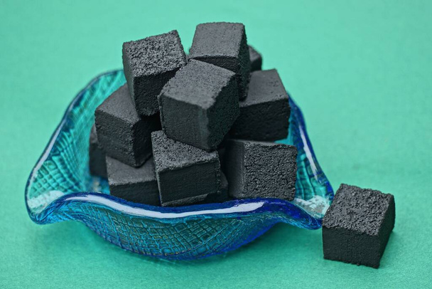 uma pilha de carvão quadrado preto para um narguilé em um cinzeiro de vidro azul fica em uma mesa verde - Foto, Imagem