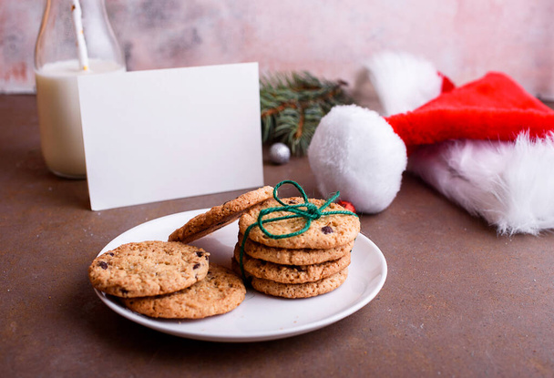 Смачне печиво з шоколадом на білій тарілці, молоко, Санта-капелюх, наклеєне на текст. Лист і печиво для Санти. Зміст свят
 - Фото, зображення