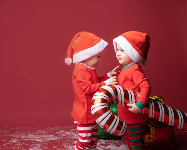 two toddler boys brothers twins in red Santa hat with Xmas candy cane on a red background. - Foto, Bild