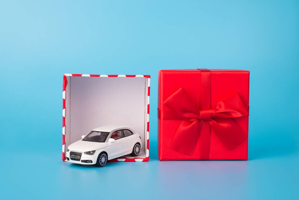 Donner et recevoir des cadeaux concept. Photo rapprochée de voiture jouet blanc en boîte cadeau rouge ouverte avec arc isolé sur fond bleu - Photo, image