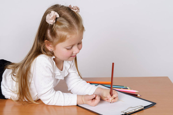 Children concept. The girl lies and draws on a sheet of paper with pencils. Isolated over white background. - Φωτογραφία, εικόνα