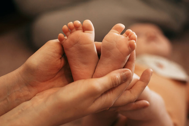 Η μητέρα κρατά τα πόδια του μωρού στα χέρια της. - Φωτογραφία, εικόνα