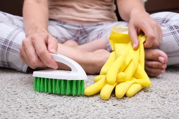 Woman in yellow gloves with a green brush is so tired of cleaning and brushing carpet, removing stains and wool from it and doing routine homework, that she sat down on the floor and rest. - Φωτογραφία, εικόνα