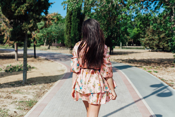Belle femme brune dans une robe avec des fleurs se promène dans le parc seul - Photo, image