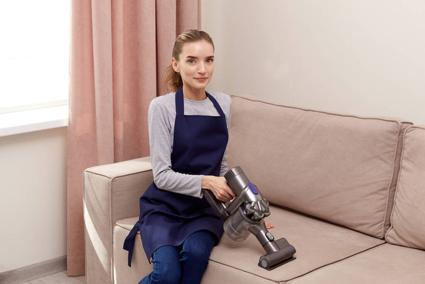 A young woman vacuums the sofa with a cleaning vacuum cleaner. - Photo, image