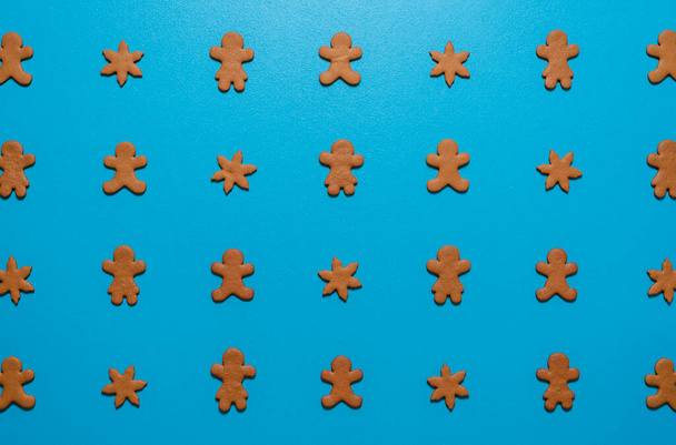 Üzerinde ev yapımı zencefilli kurabiyeler var. Mavi renkli bir masada simetrik olarak sıralanmış. Zencefilli adam ve kadın mavi arka planda yatıyorlardı. - Fotoğraf, Görsel