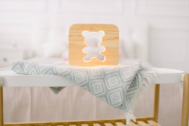Night lapms and decor. Home interior and cozy accessories. Wooden lamp with bear cut out picture, on table, at beautiful light bedroom at home - Photo, image