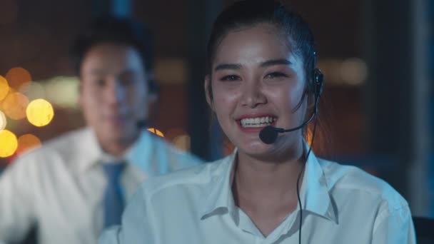 Millennial Asia genç çağrı merkezi ekibi ya da müşteri destek servisi yöneticisi bilgisayar ve mikrofon kulaklığı kullanarak gece geç saatlerde ofiste çalışıyor. Tele pazarlama ya da satış işi kavramı. - Video, Çekim