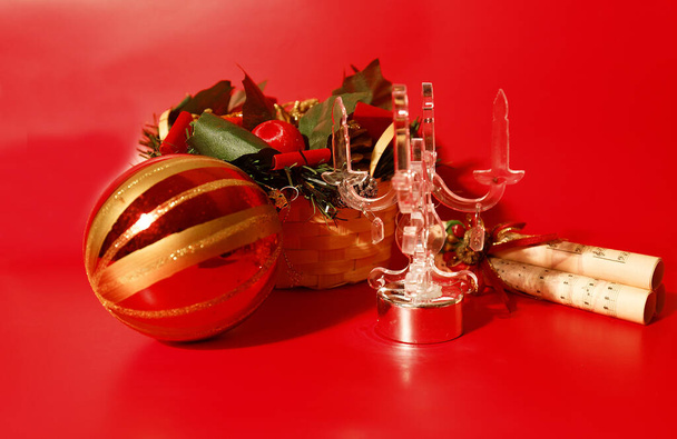 Karácsonyi lakberendezés üveg gyertyatartóval, karácsonyi csecsebecse, pergamen és kosár piros háttér. - Fotó, kép