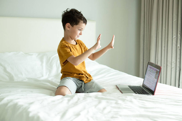 El niño feliz muestra diez en los dedos. Clase de matemáticas preescolares en un dormitorio blanco con una computadora portátil. Cara excitada. El concepto de una escuela en casa, aprendizaje a distancia en línea, las tecnologías modernas de la educación. Luz de día - Foto, imagen